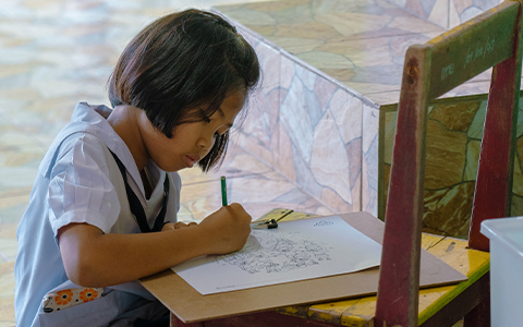 Promo image showing a young girl writing on a piece of paper and hopeful for her education