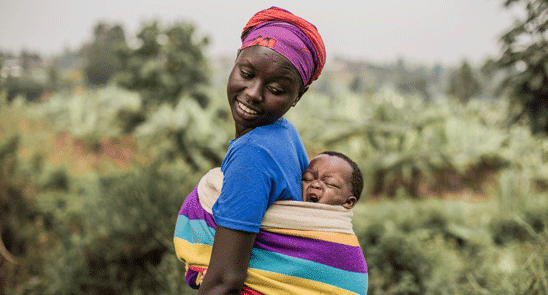 Mother smiles over her shoulder at her baby swaddled on mom's back