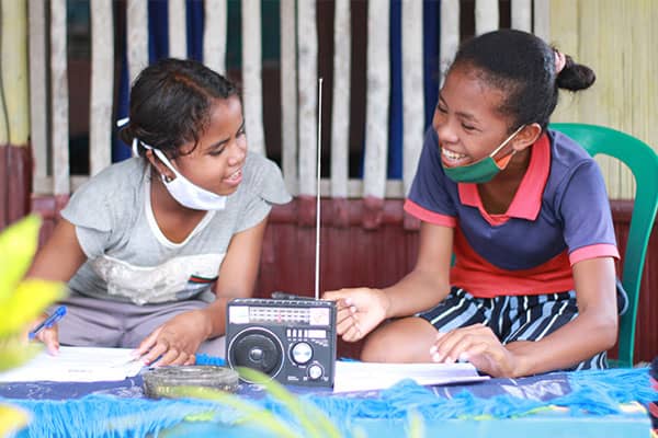 Two girls in Indonesia, both named Maria, listening to a radio remote learning lesson together