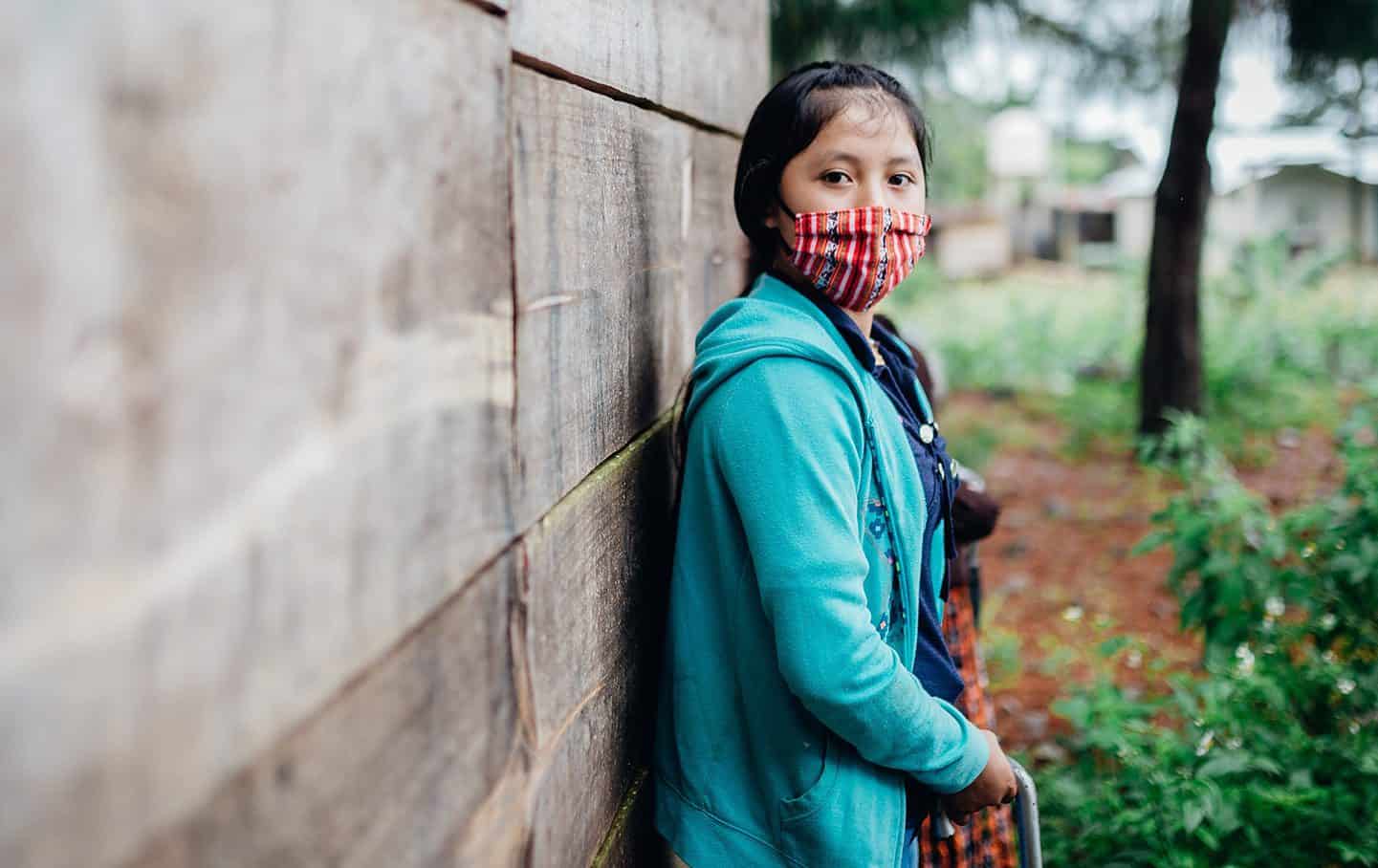 A woman in a mask looks at the camera