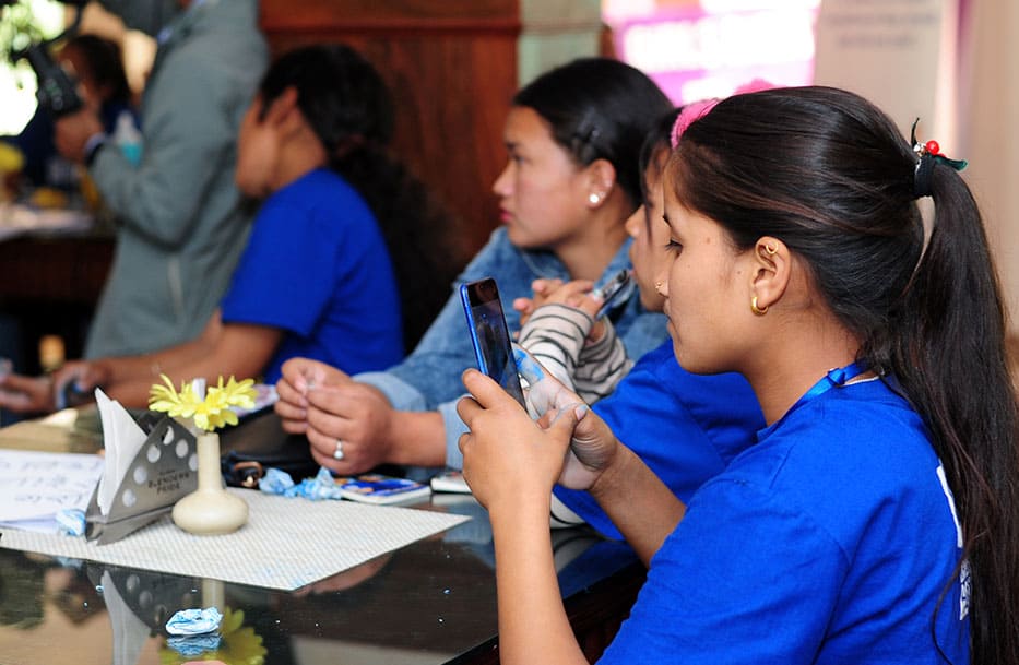 Young women together, using social media on a smartphone, to learn about child marriage spike during COVID-19 pandemic