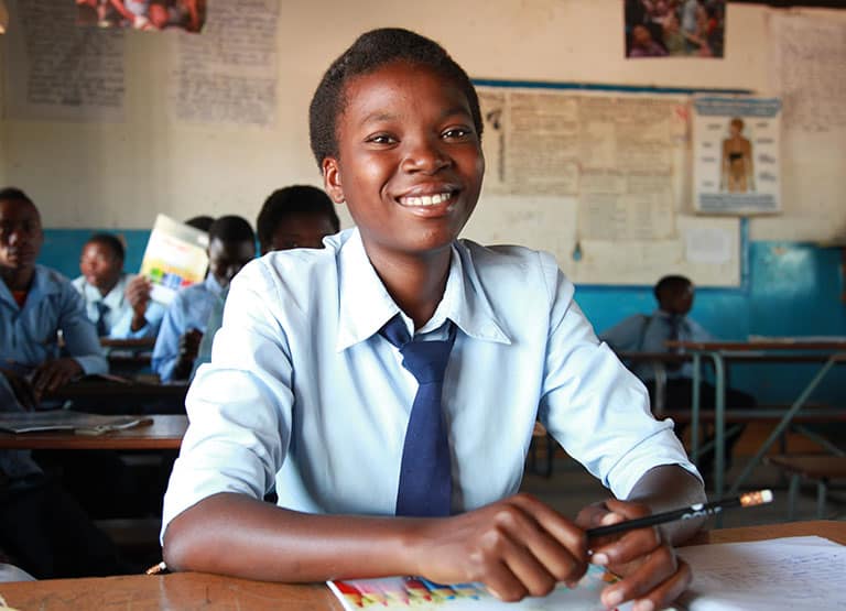 A teen girl in her school uniform smiles from her classroom