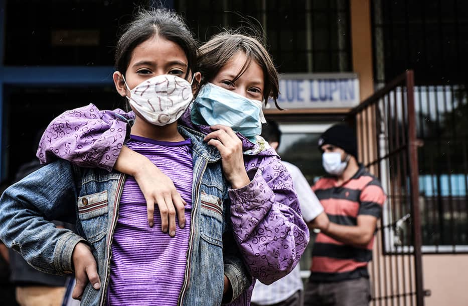 Two girls hugging wearing masks