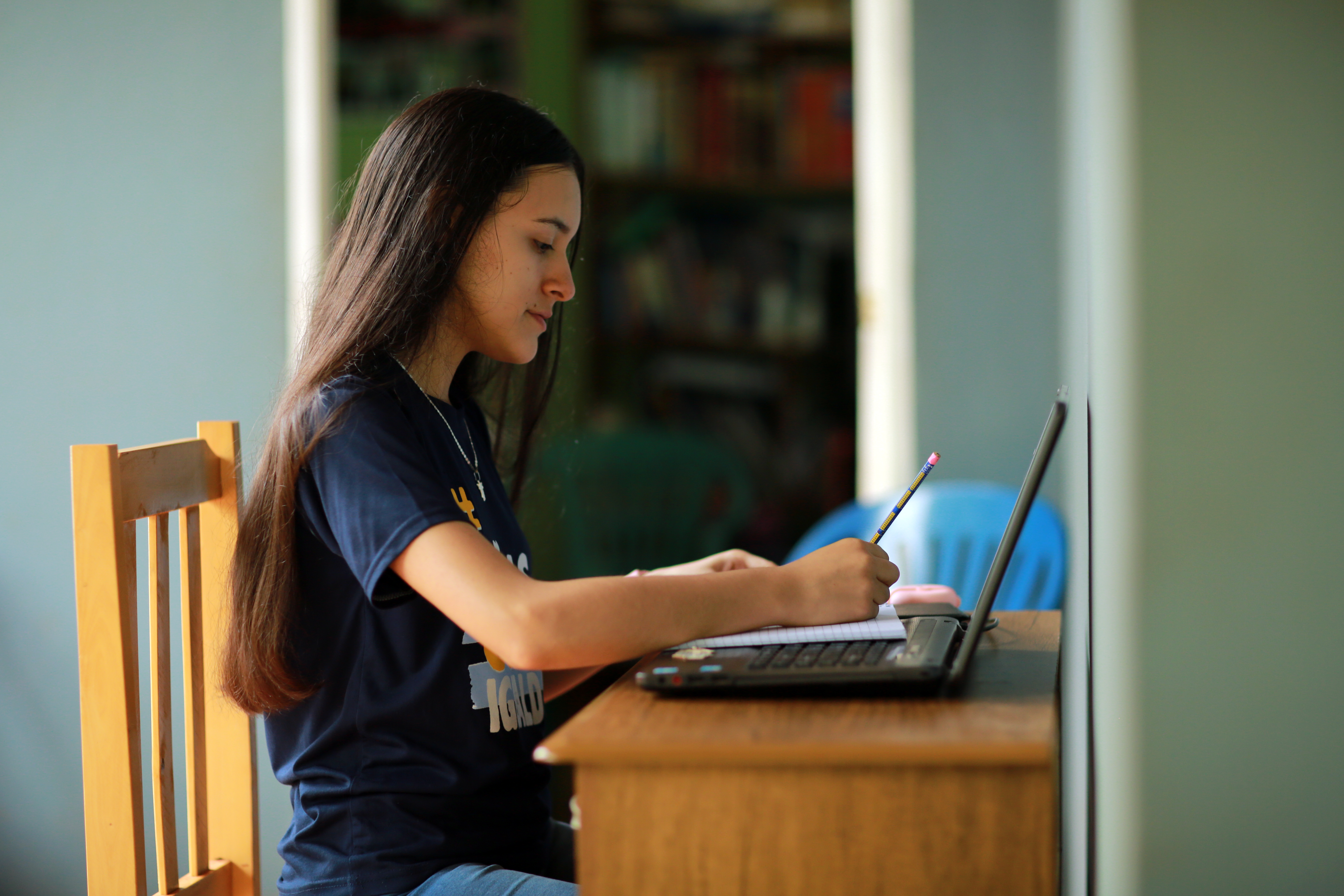 A young woman writes in a notebook with her laptop open