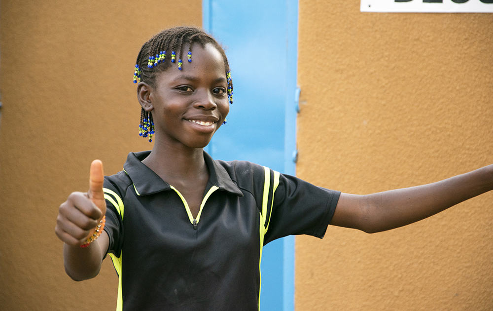 Awa, 13, gives a thumbs up as she stands outside of the new block of latrines that her school installed with Plan’s support. 