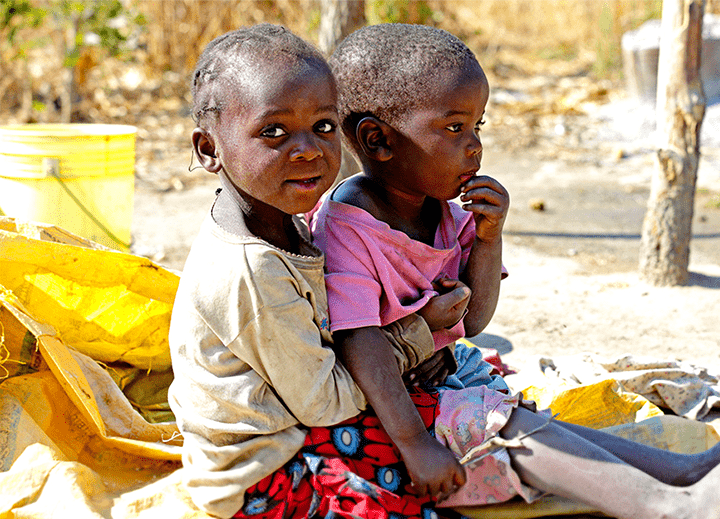 Two young children sitting in the foreground of a dry, barren looking landscape.