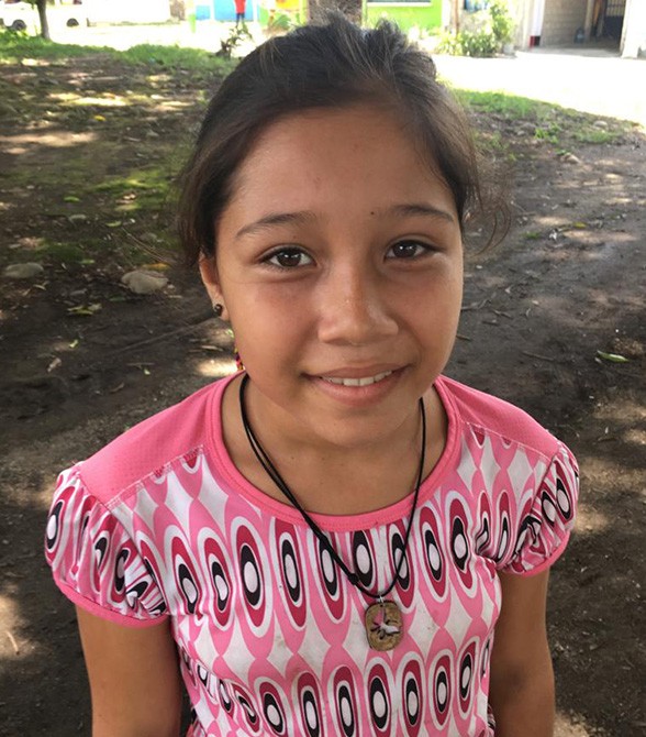 Young girl smiling for camera wearing a pink shirt.