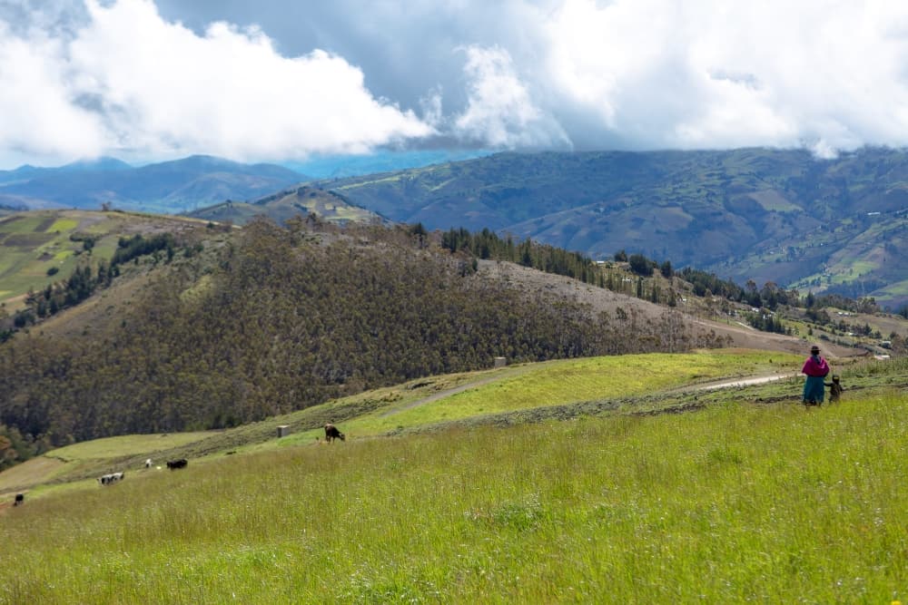 A woman and her young child stand along rolling hills of the Andes mountain region in Ecuador.