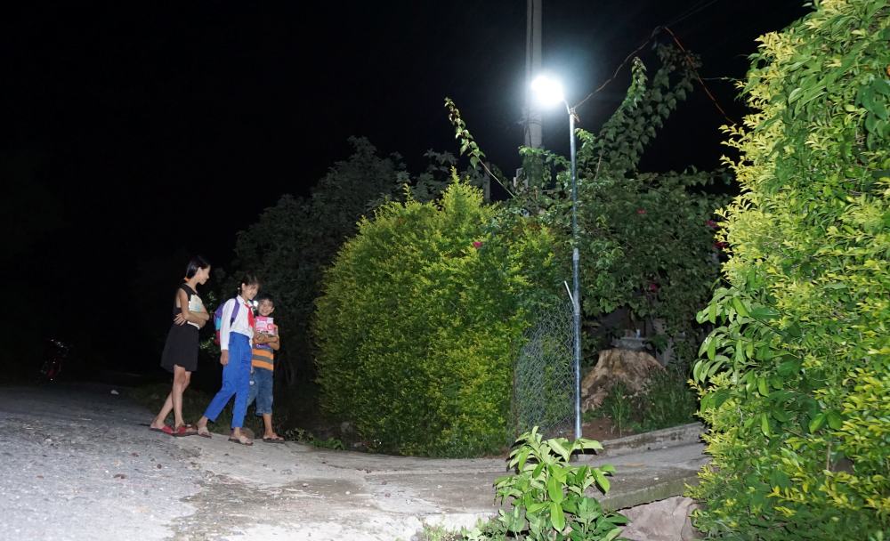 Three young people walk along a newly lit pathway in their village.