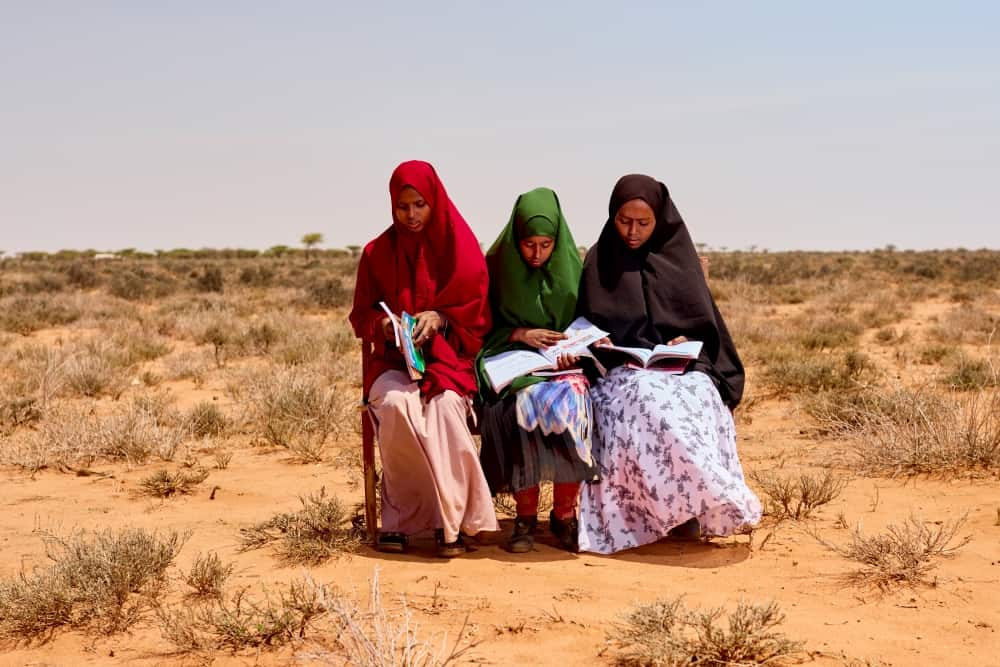 ZamZam, Juweriya and their friend Habbiq sit together on a bench and read through some school materials.