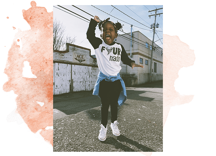 A small child with two top buns happily jumps with their hand raised high! Plan International USA partnering with Unsplash.