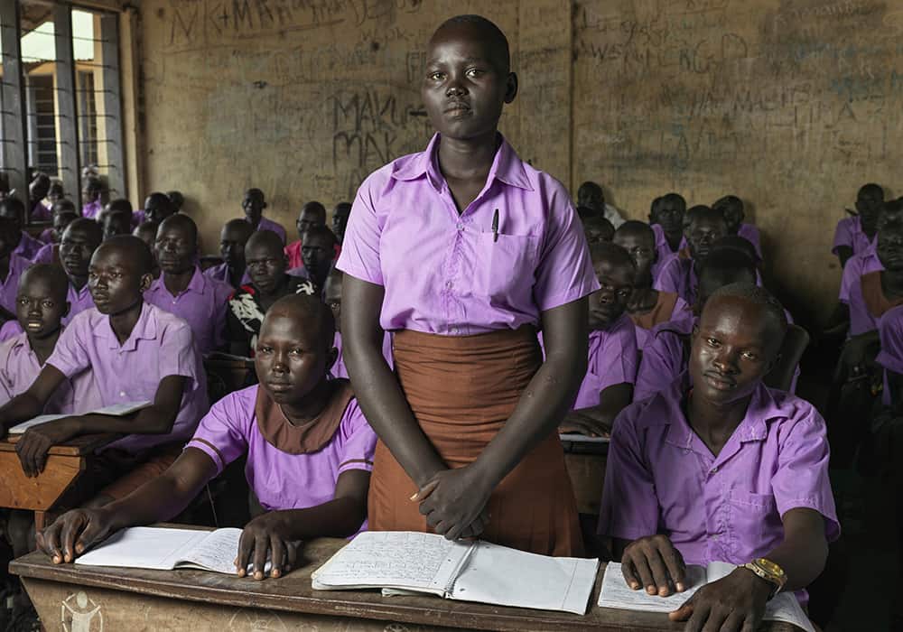 Hellena stands in her classroom in South Sudan. “[When my family and I] eat only once a day, in the evening,” she says. “But in the morning and lunch time, we don’t eat. … we eat pumpkin leaves, it’s the only plant that survived the drought, but it doesn’t bear any fruit.”