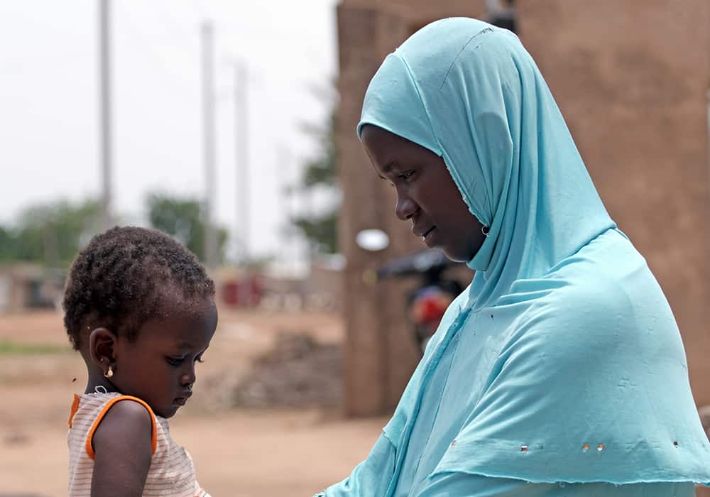 A mother who was forcibly displaced from her home sits with her young daughter in Koupela. 