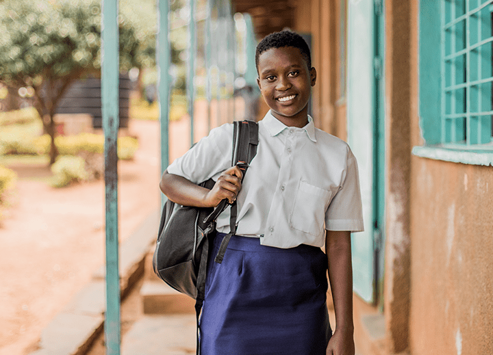 Young girl smiling and holding backpack strap slung over shoulder. Plan International USA