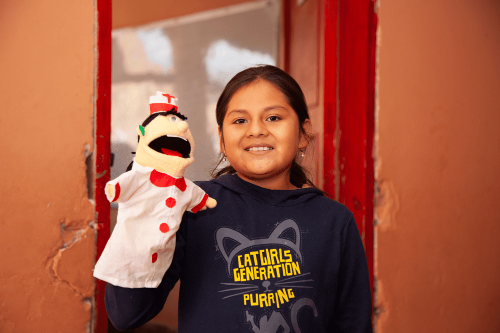 A girl in Bolivia smiles at the camera while holding up a hand puppet.