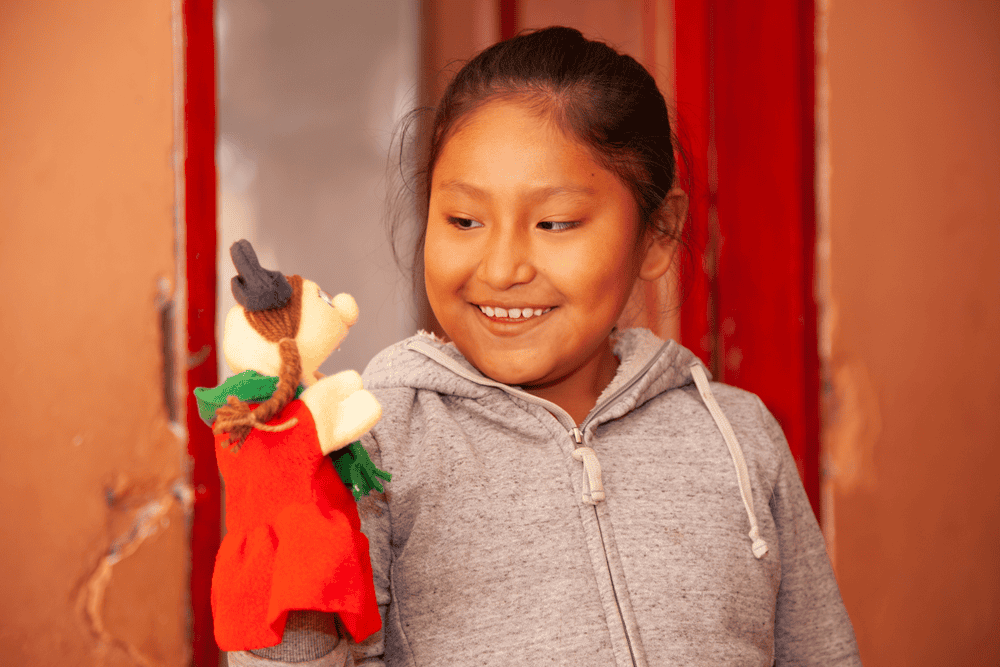 A girl in Bolivia smiles at the hand puppet she is holding.