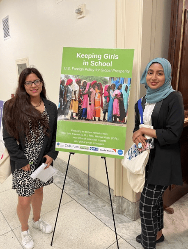 Rida and Nataly stand next to a poster that promotes the Keeping Girls in School Act. 