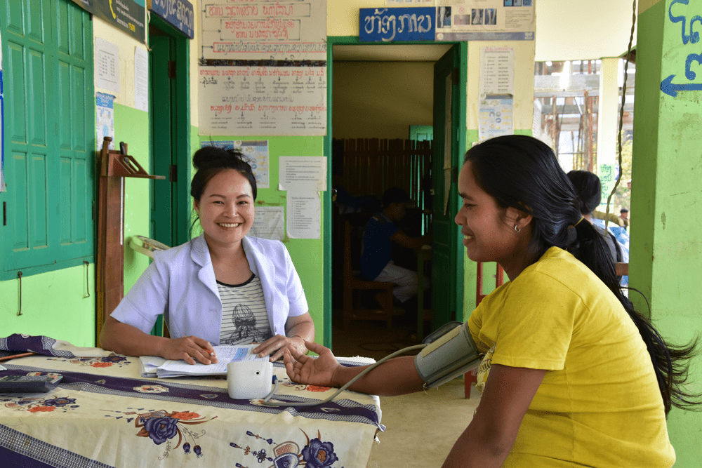 A nurse at the health center in Laos smiles while taking the blood pressure of a young pregnant woman.
