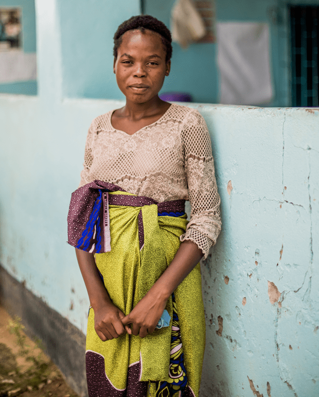 Keira, a pregnant woman in Zambia, leans against a pale blue wall.