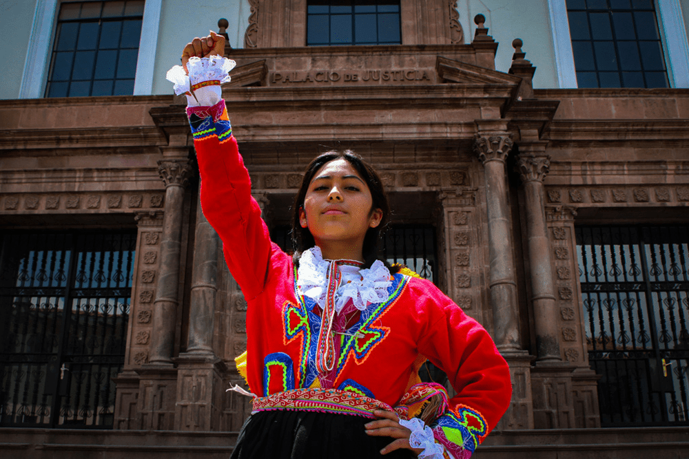 A girl in a colorful red top with a ruffle neck holds her fist in the air.