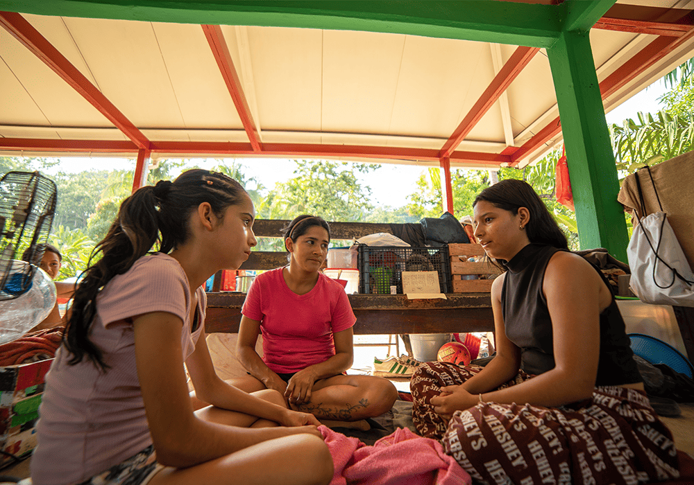 Carmen, her sister and her mother sit together on the floor.