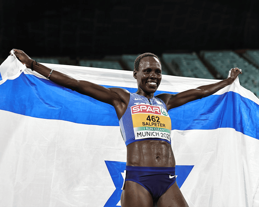 Kenyan-Israeli runner Lonah-Chemtai Salpeter celebrates after competing in Munich, holding up the blue and white Israeli flag behind her like a cape.