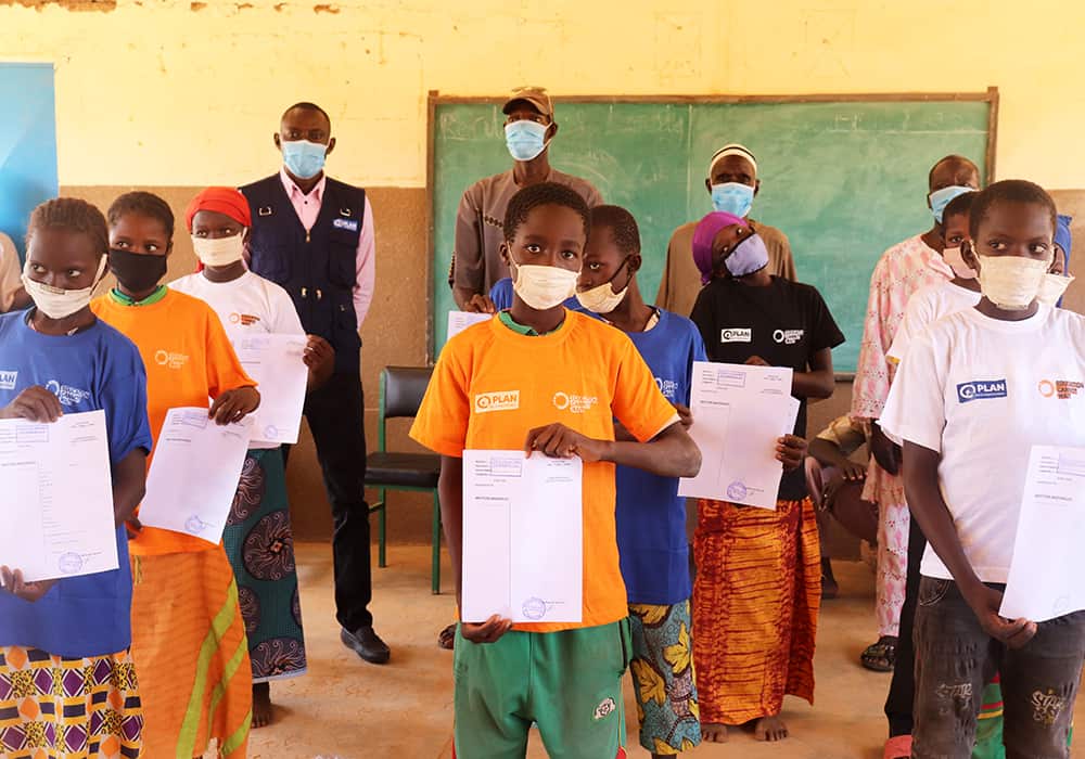 Children in a classroom hold up their birth certificates at the hand-over ceremony.  