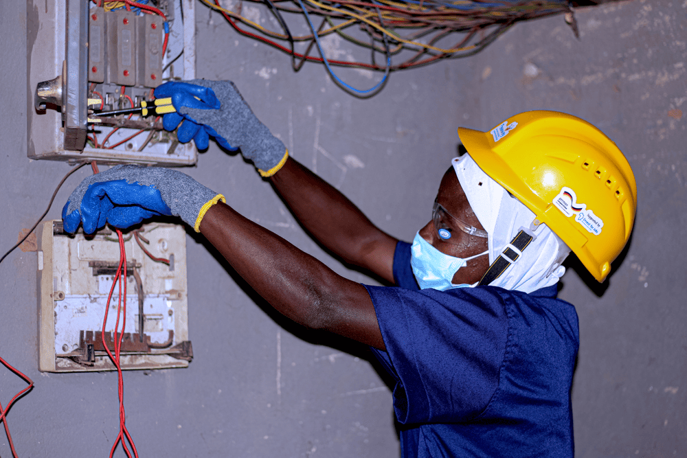 Nashira, a young woman from Ghana, wears a helmet, face mask and gloves as she repairs a circuit breaker.