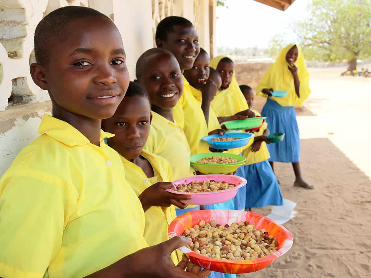 Girls line up in the shade after receiving lunch at school.