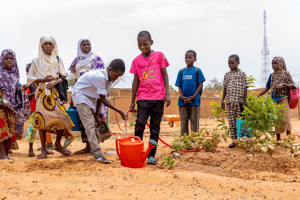 A group of boys and girls stand together in the school garden in Niger.