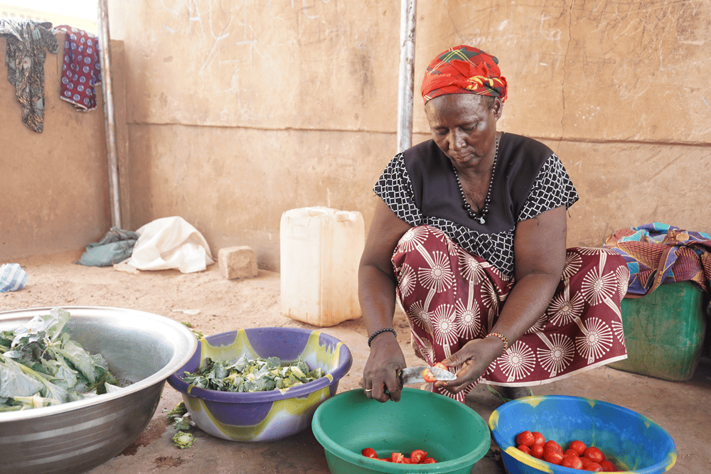 A woman prepares large bowls of vegetables, including tomatoes and cabbage. 