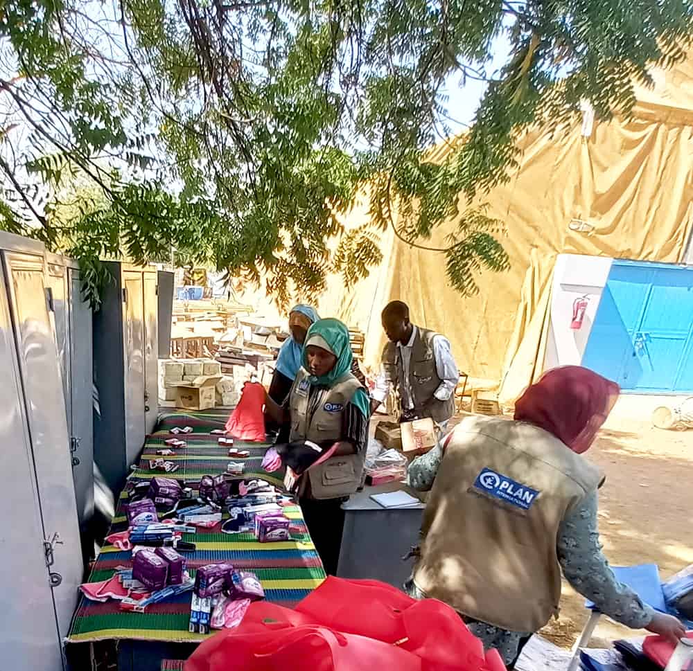 Plan Sudan staff in brown vests sort through supplies on a long table outside.