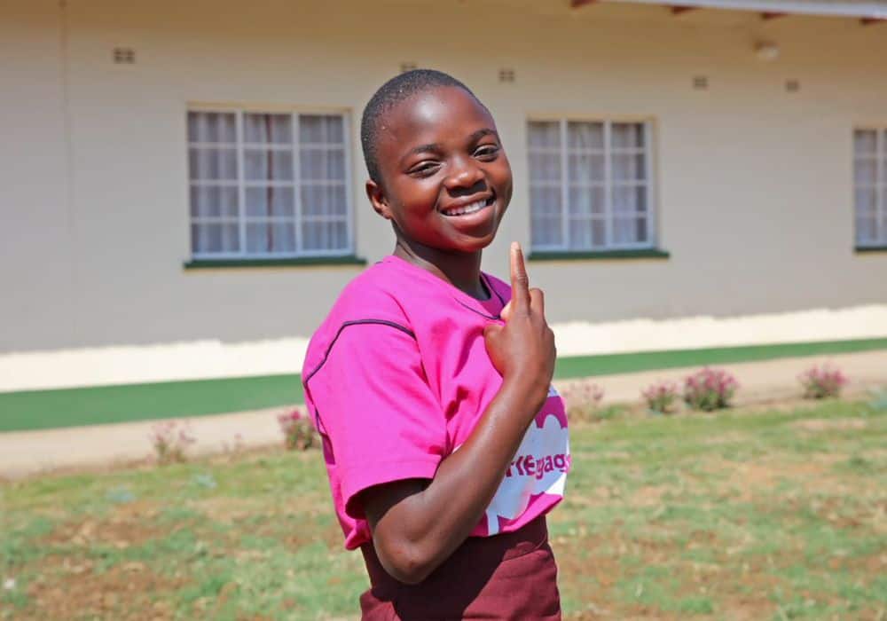 Nokuthula smiling in her school’s courtyard, wearing a pink GirlEngage shirt. 