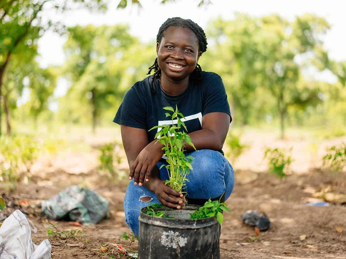 A girl kneels beside a plant in Ghana.