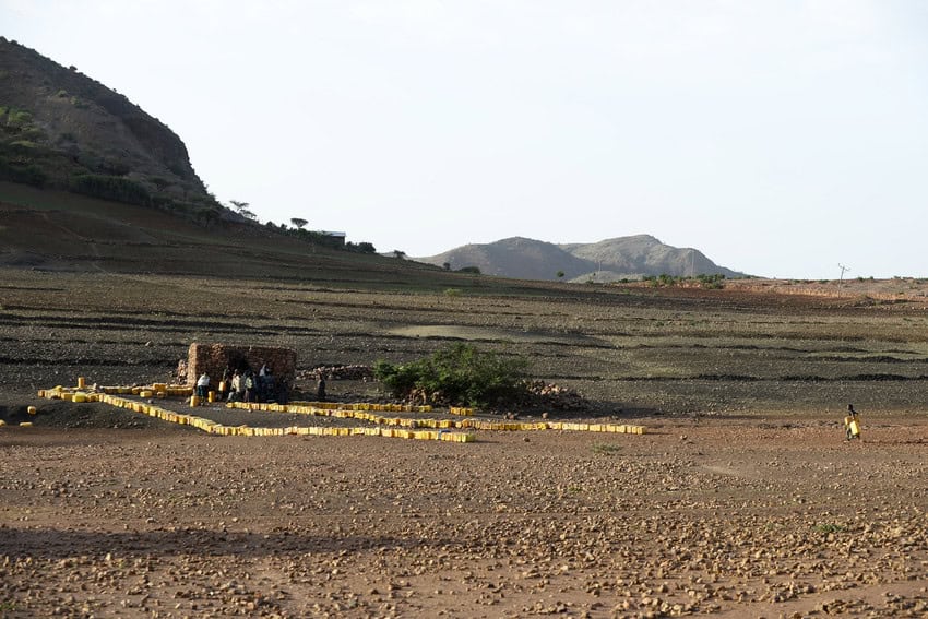 Hundreds of yellow jerry cans stand out against the expanse of dry brown earth around the water tank. 