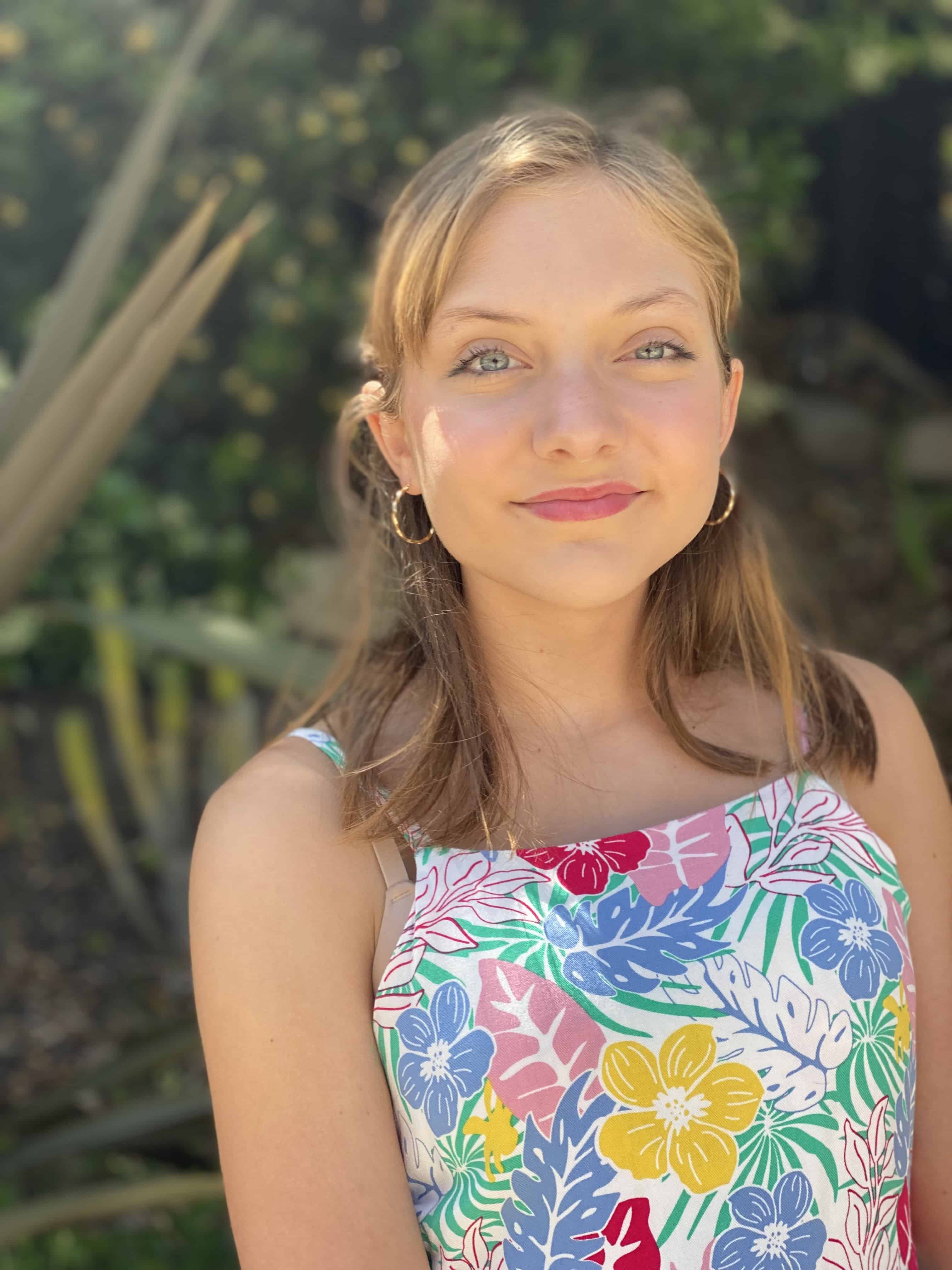 Lily, a young White woman with blonde hair, looks at the camera with a closed-mouth smile.