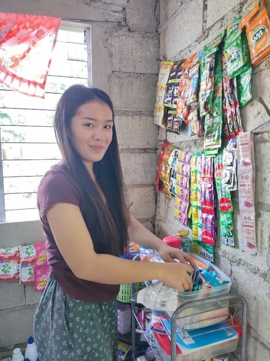 A young woman in the Philippines smiles at the camera as she unpacks inventory in her store.