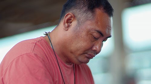A man wearing a red shirt leans forward while looking down.