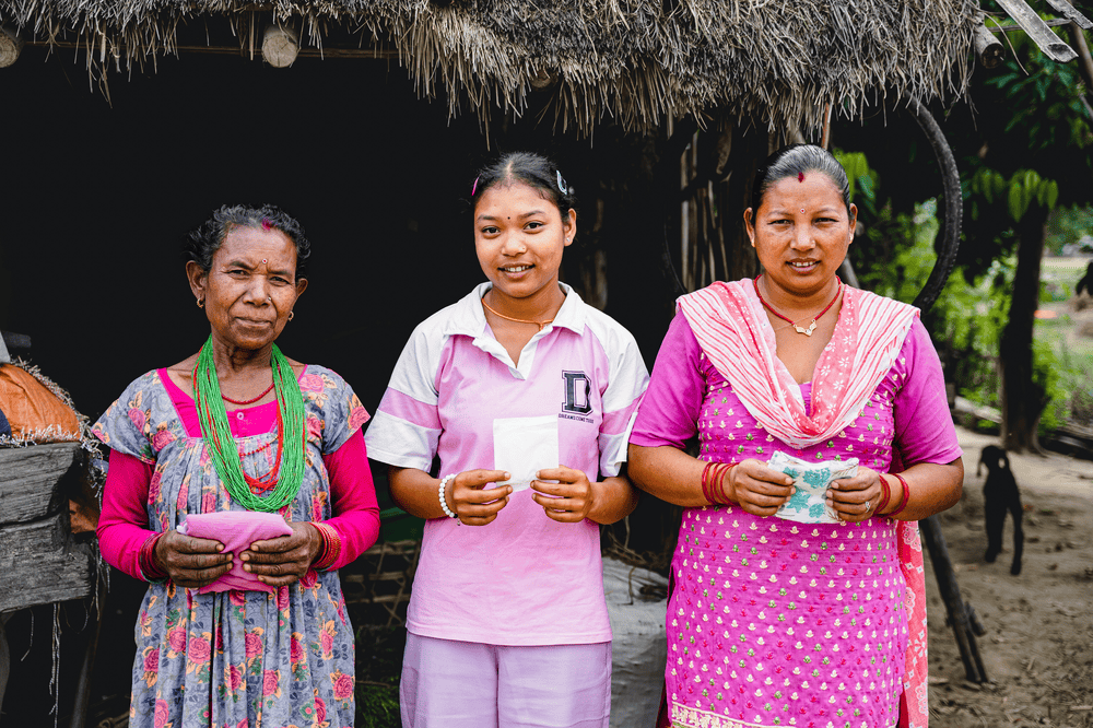 Tilki, Rita and Pushpa stand side by side and hold up menstrual pads.