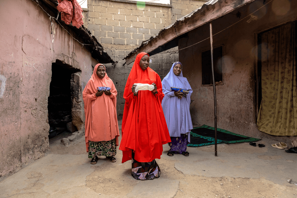 Teenager Rahamatu stands in front of her mother Sakina and grandmother Rahamatu, who all hold examples of menstrual pads their unique generations use in Nigeria.