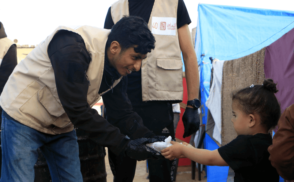 Palestinian aid worker hands young girl a plate of food.