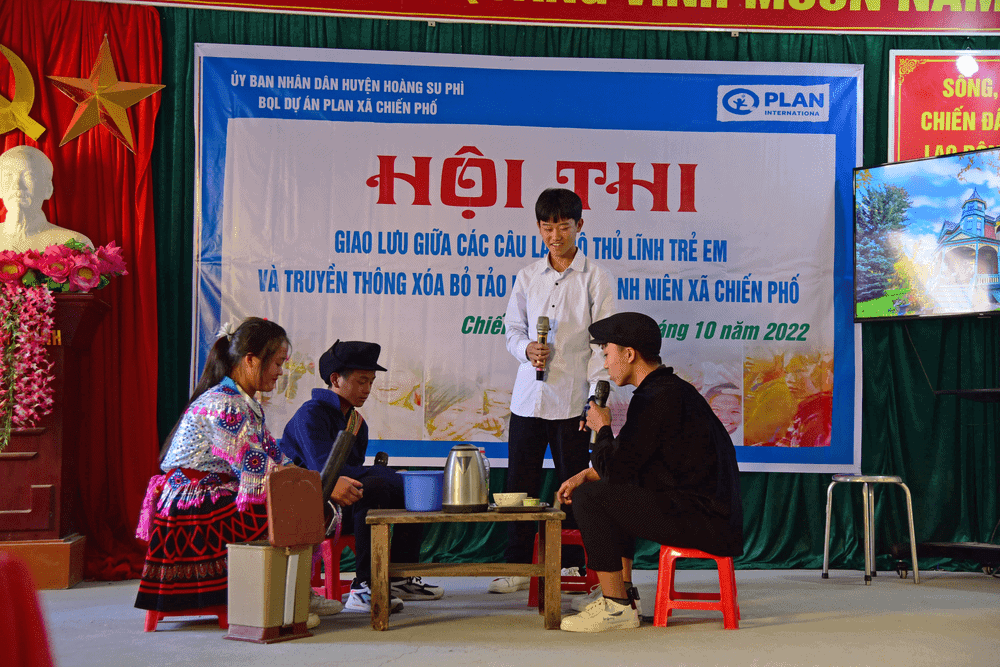 Four young people sitting around a small table in front of a sign written in Vietnamese.