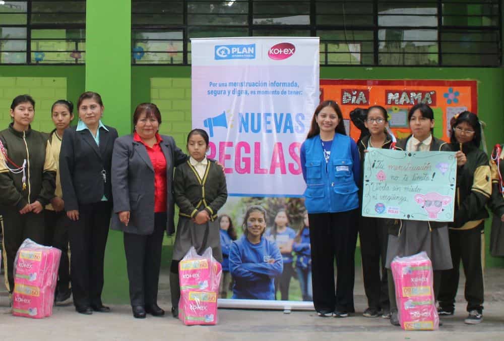 Girls in Peru stand in front of a Plan banner with the menstrual health kits they received.
