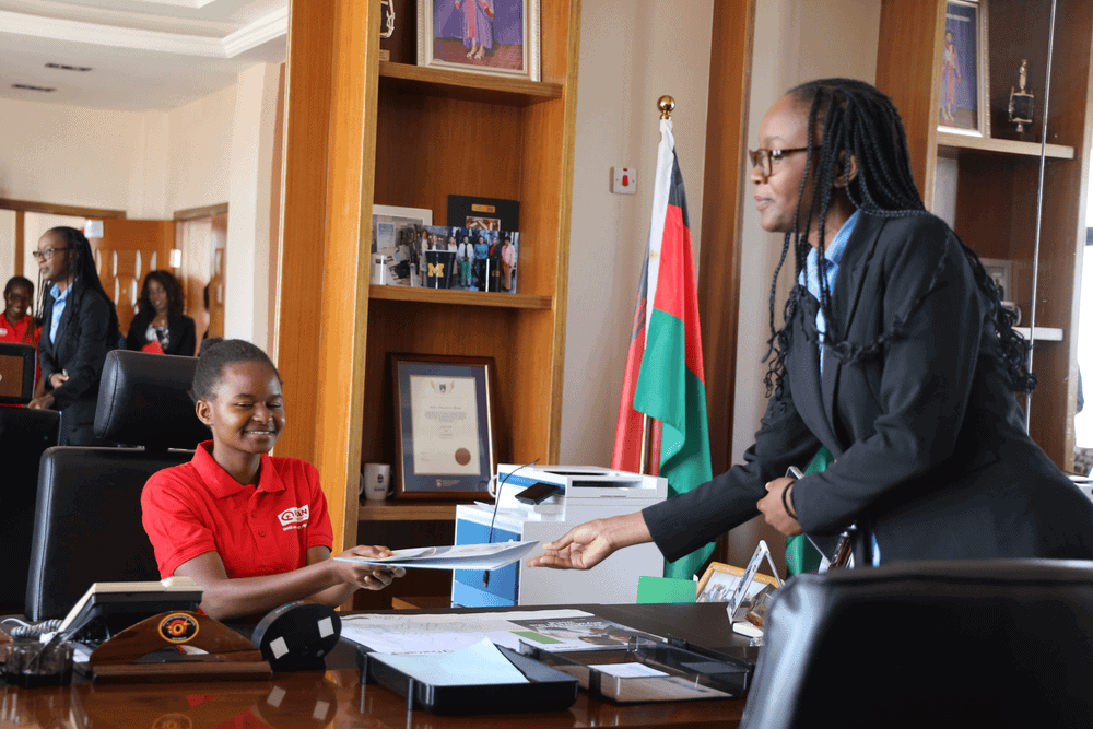 Dr. Chirwa Kajombo hands papers to Fanny who sits at her desk.