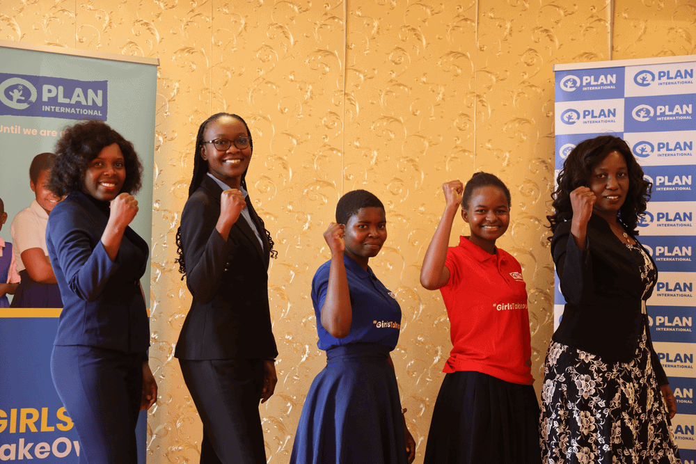Two young women stand and hold up their arms alongside three members of the Malawi University of Science and Technology.
