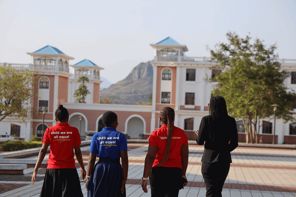 Three young women and a Malawi University faculty member face away from the camera as they walk outside.