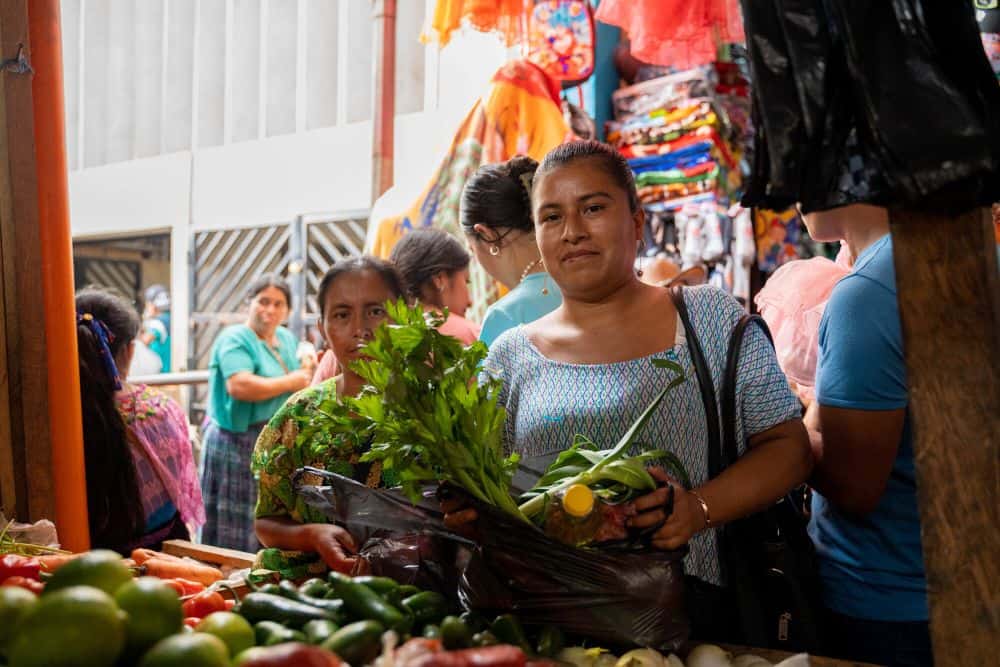 A woman collects vegetables at an outdoor market.