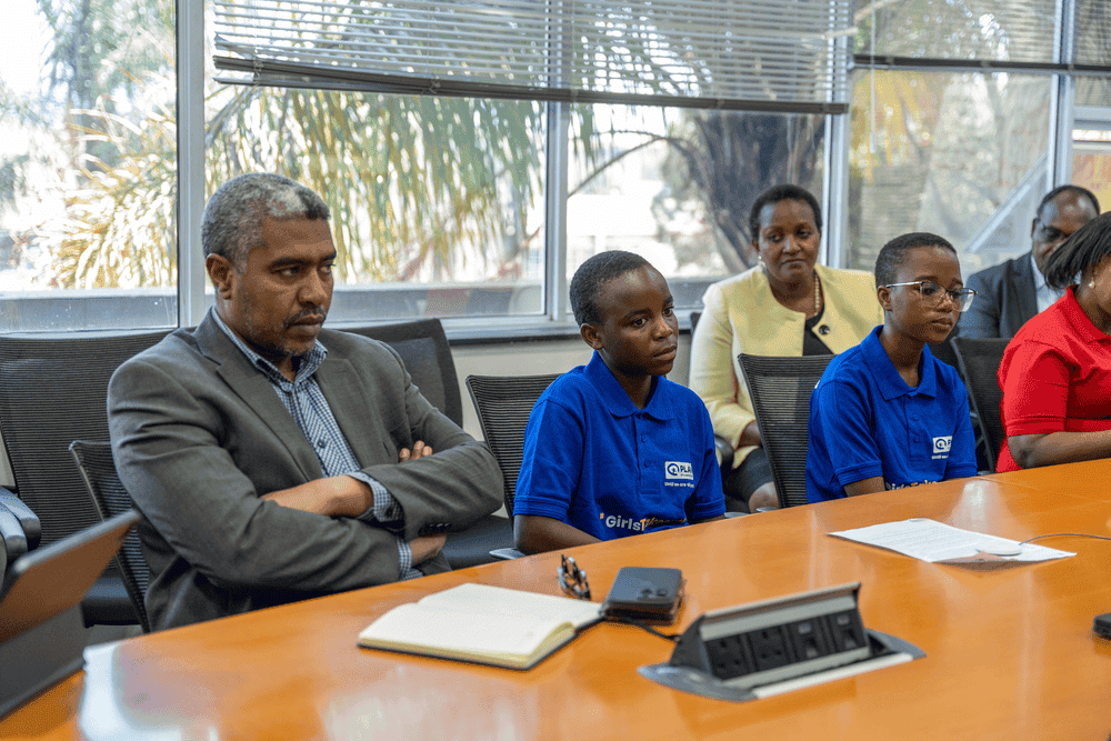 Two girls wearing blue t-shirts sit at a table next to staff on the education team at the World Bank.