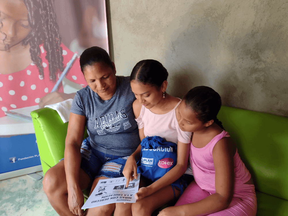 Teen girls sits on a couch between her mom and sister to talk about menstrual health.