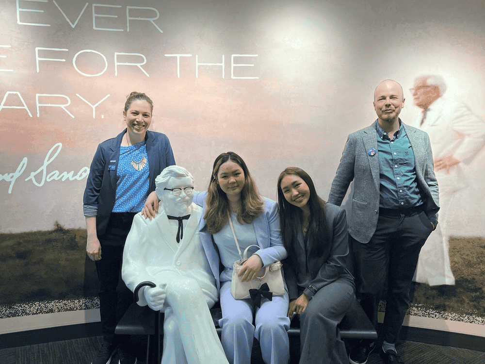 Pear and Shirlyn sit next to a Colonel Sanders statue with Plan staff on either side of them.